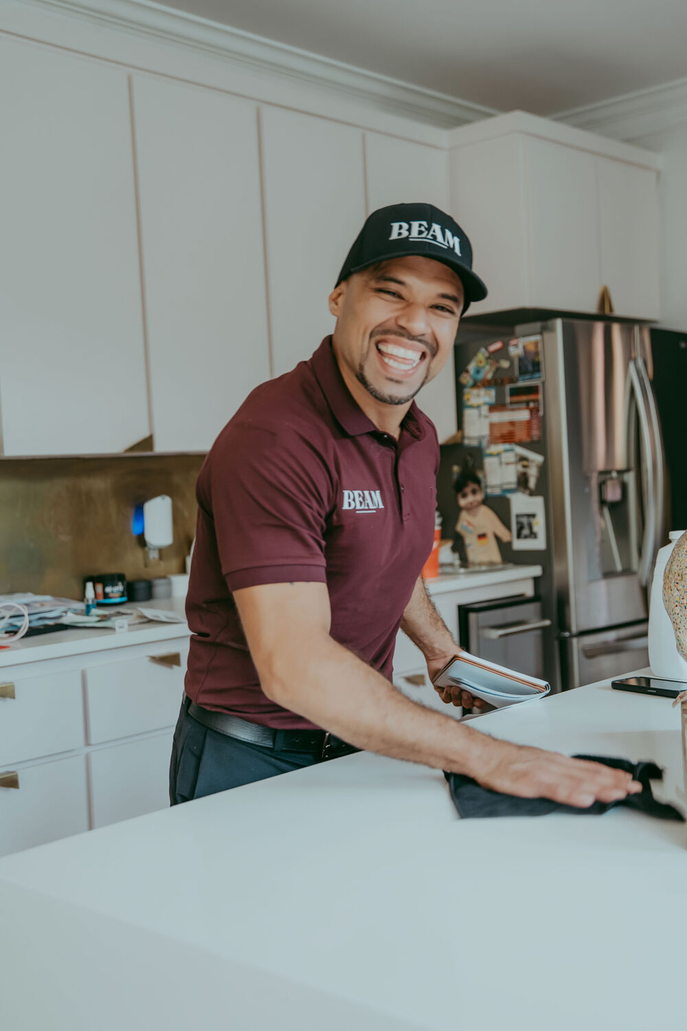 A smiling Beam team member in a maroon polo and Beam cap wiping down a kitchen counter