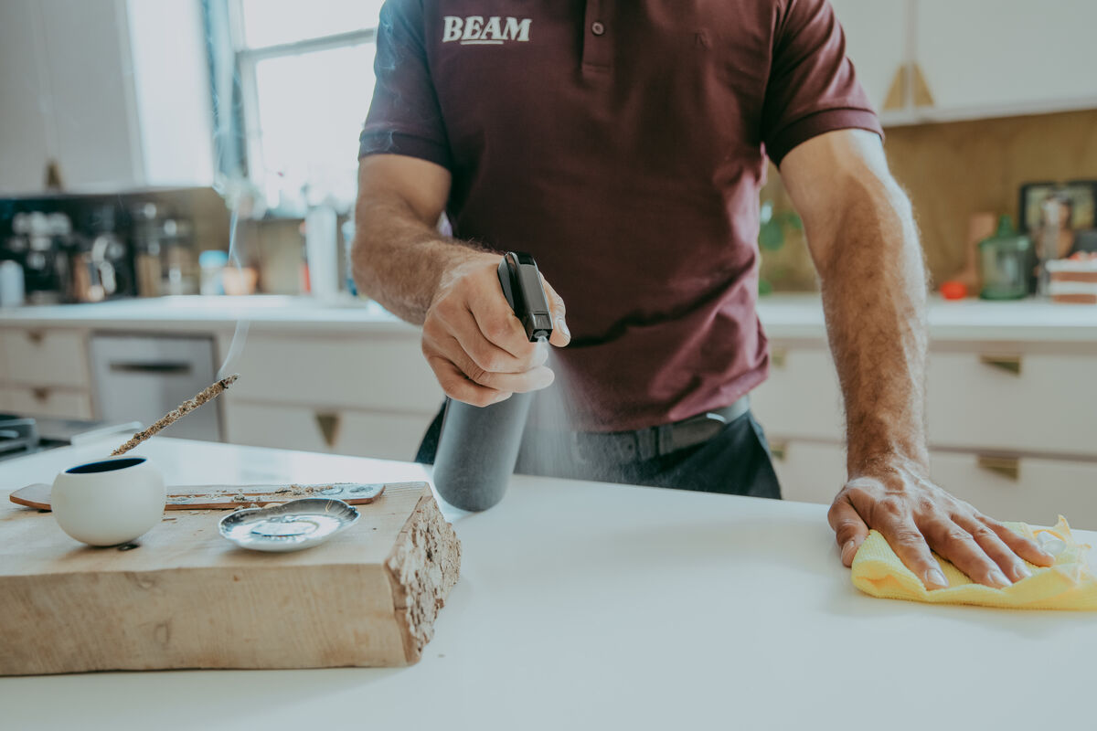 Beam team member spraying and wiping a kitchen counter with non-toxic cleaner