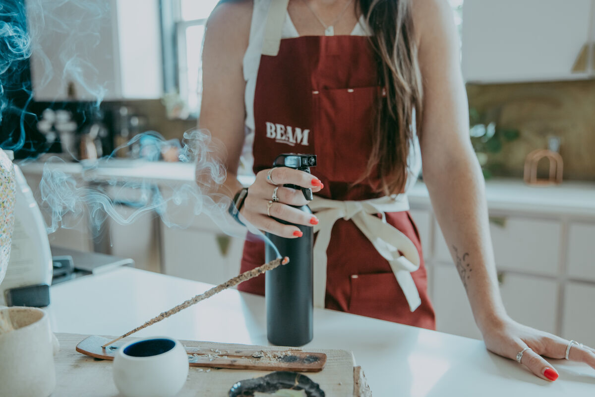 A Beam team member in a maroon apron finishing a kitchen reset as incense smoke drifts across the counter